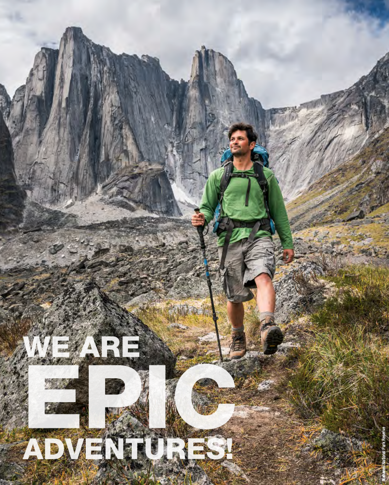 DESCRIBING: A medium, vertical photograph.

A visitor dressed in beige shorts, brown hiking boots, a bright green long sleeved shirt and wearing a big blue backpack is seen hiking in a mountainous region in Nahanni National Park. The hiker is looking off to one side smiling and is using a hiking pole, which is grasped in one hand.

Behind the hiker gray rocky cliffs rise up sharply into the sky, which is dominated by white fluffy clouds with only a small patch of blue sky showing at the top right corner. At the base of the rock face to the right of the hiker, short yellow grass creeps up the base of the cliff side and continues into the foreground where it meets the route the hiker is travelling upon. To the left of the hiker is a big grey boulder and to the right longer green grass grows.

CAPTION: Nahanni National Park Reserve

RELATED TEXT: We are epic adventures!